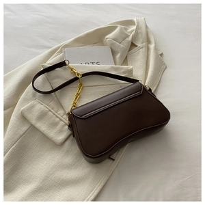 Detail of dark brown leather baguette bag with gold chain strap on a cream blazer