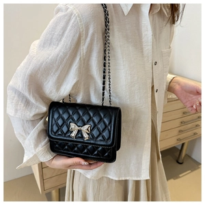 Close-up of a black quilted shoulder bag with a silver bow accent on a female model