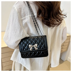 Close-up of quilted shoulder bag with silver bow accent and metal chain strap