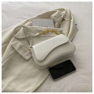 Close-up of a white saddle bag with a chunky gold chain handle on a beige blazer