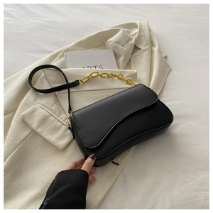 Close-up of black leather shoulder bag with gold chain over white blazer on fabric