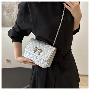 Detail of silver quilted crossbody bag with a metal bow buckle and fine chain strap