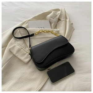 Detail of black leather crossbody bag with gold chain strap on a beige blazer