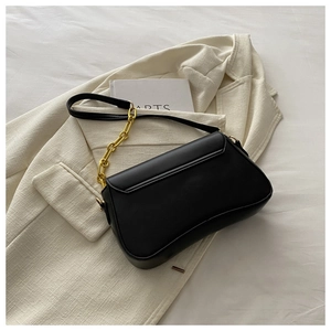 Detail of minimalist black underarm bag with gold chain strap on blazer background