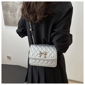Silver quilted shoulder bag with metal bow detail worn by a model in a minimal setting