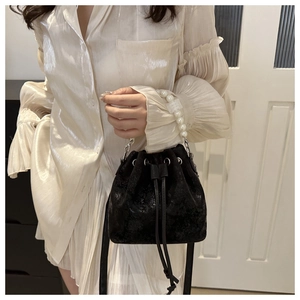 Close-up of textured black bucket bag featuring elegant large pearl handles and drawstring