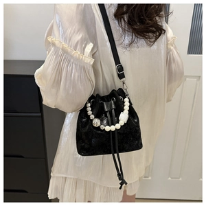 Detail of black drawstring bucket bag with pearl handle and leather strap on model