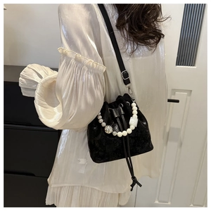 Détail du sac seau noir avec anse en perles porté avec une robe en soie blanche