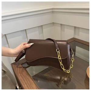 Detail of dark brown leather crossbody bag with gold chain and curved bottom edge