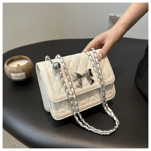 Detail of white quilted chain bag featuring a silver metal bow buckle and elegant side ball charm