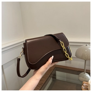 Close-up of dark brown PU leather crossbody bag with gold chain and curved flap