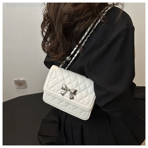 Model showing white quilted crossbody bag with silver bow detail and chain strap