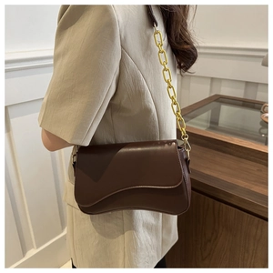 Detail of dark brown leather bag featuring wave-edge flap and golden chain strap link