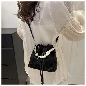 Detail of a glossy black crackle texture bucket bag with pearl and metal ball handle