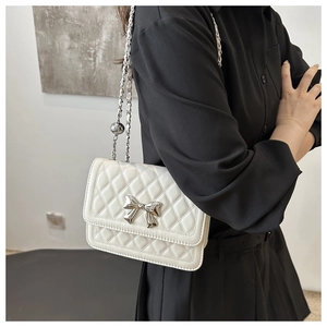 Detail of white quilted crossbody bag with silver bow clasp and chain strap