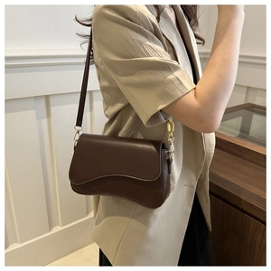Detail of a dark brown crossbody bag with a curved flap and gold chain on a female model