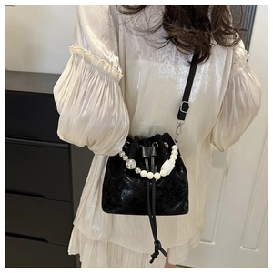 Detailed view of a black drawstring bucket bag with pearl and metallic bead handle strap