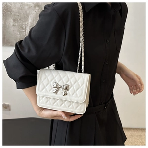 Detail of white quilted crossbody bag with silver metal bow and elegant chain strap