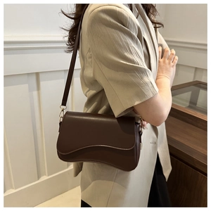 Detail of dark brown leather underarm bag with curved wave flap and gold hardware