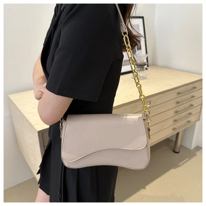 Close-up of beige leather crossbody bag with chunky gold chain strap on a model