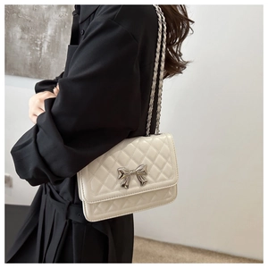Detail of quilted beige shoulder bag with silver metal bow and chain leather strap