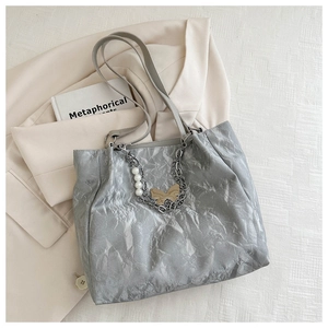 Detail of silver tote bag featuring pleated texture, pearl accents, and golden butterfly