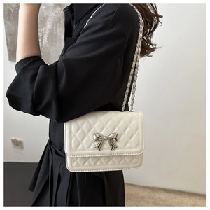 Model wearing a white quilted crossbody bag with a silver bow and metal chain strap