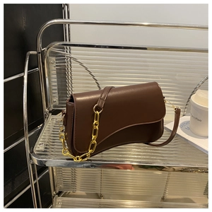 Detail of a dark brown crossbody bag with a curved flap and a chunky gold chain strap