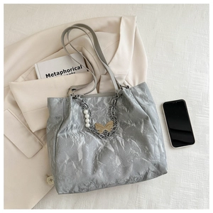 Grey pleated tote bag with pearl and golden butterfly charms on a soft fabric backdrop