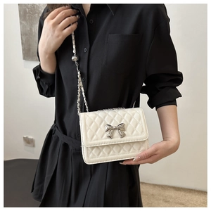 Close-up of beige quilted bag featuring a silver bow buckle and elegant metal chain strap