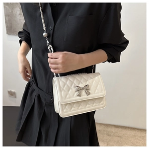 Detail of white quilted crossbody bag with silver bow accent and metal chain strap