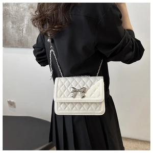 Detail of white quilted crossbody bag with silver bow buckle and chain strap shown on model