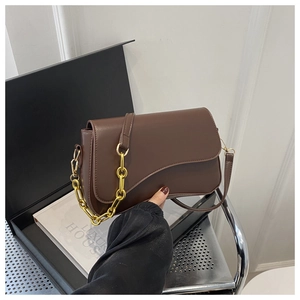 Close-up of dark brown leather crossbody bag with curved flap and gold chain detail