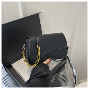 Close-up of black matte saddle bag with chunky gold chain detail and leather strap