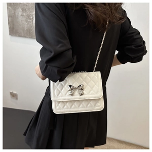 Detail view of a white quilted crossbody bag with silver bow accent and chain strap