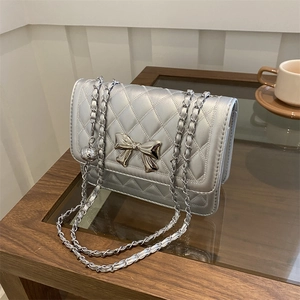 Detailed close-up of a silver quilted chain bag with a metallic bow and ball charm