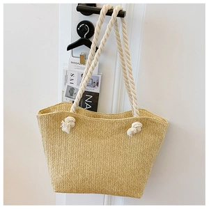 Detail of straw woven tote bag featuring white rope handles and decorative knots