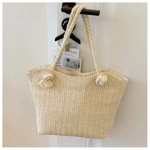 Detail of hand-woven straw tote bag with chunky cotton rope handles on a door handle