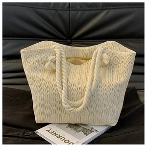 Detail of beige woven tote bag with thick cotton rope handles and tassel accents