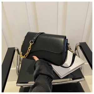 Detail of a black minimalist faux leather crossbody bag with wavy flap and gold chain strap