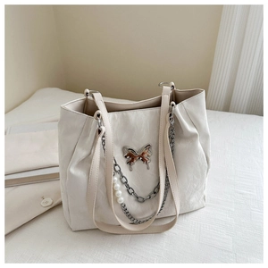 Detail view of cream white tote bag featuring decorative butterfly charm and pearl chains