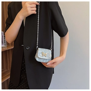 Mini sac bleu métallisé avec boucle papillon dorée porté sur une veste noire