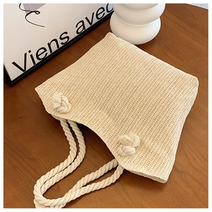 Detail of straw tote bag featuring woven texture and white cotton rope handle with knots