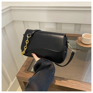 Detail of black shoulder bag featuring scalloped edge flap and gold chain strap accents