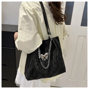 Detail of black pleated tote bag with silver chain and metal butterfly charm