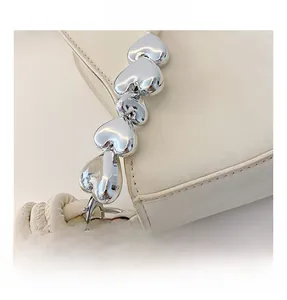 Detail of cream leather bag featuring silver heart-shaped metal chain and knotted strap