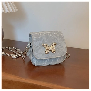 Détail du tissu plissé argenté et du fermoir papillon en métal sur un mini sac à chaîne