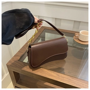 Detail of dark brown shoulder bag featuring asymmetrical flap and gold chain strap