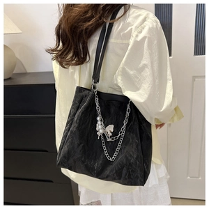 Detail of black pleated tote bag with silver butterfly chain shown on woman's shoulder
