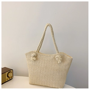 Detail of woven straw tote bag featuring rope handles and decorative tassels
